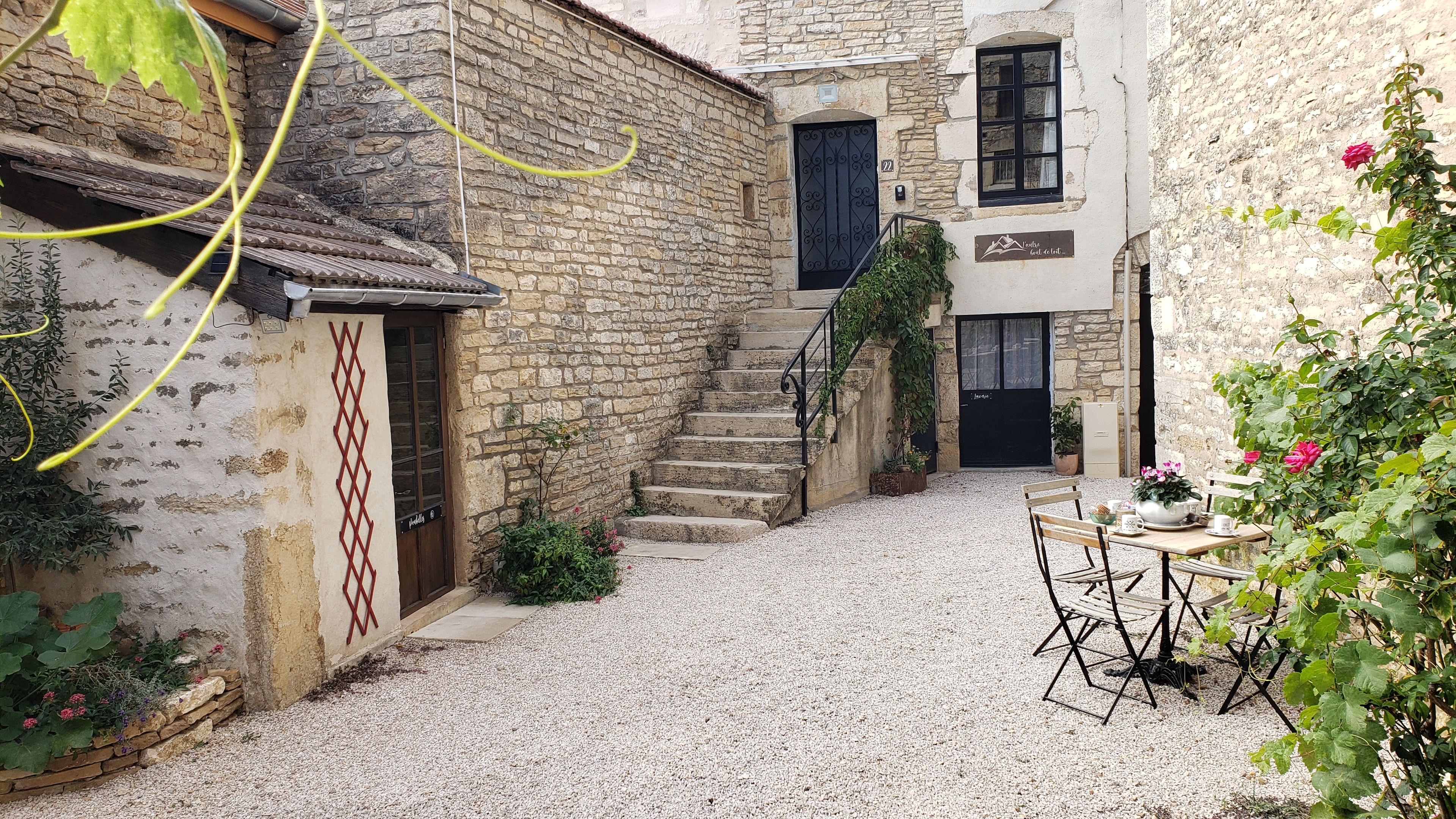 A courtyard with stone walls, a staircase, a table with chairs, and a sign indicating a restaurant.