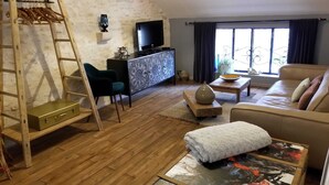 Un soggiorno con una scala in legno, un divano, una TV e una finestra con tende.