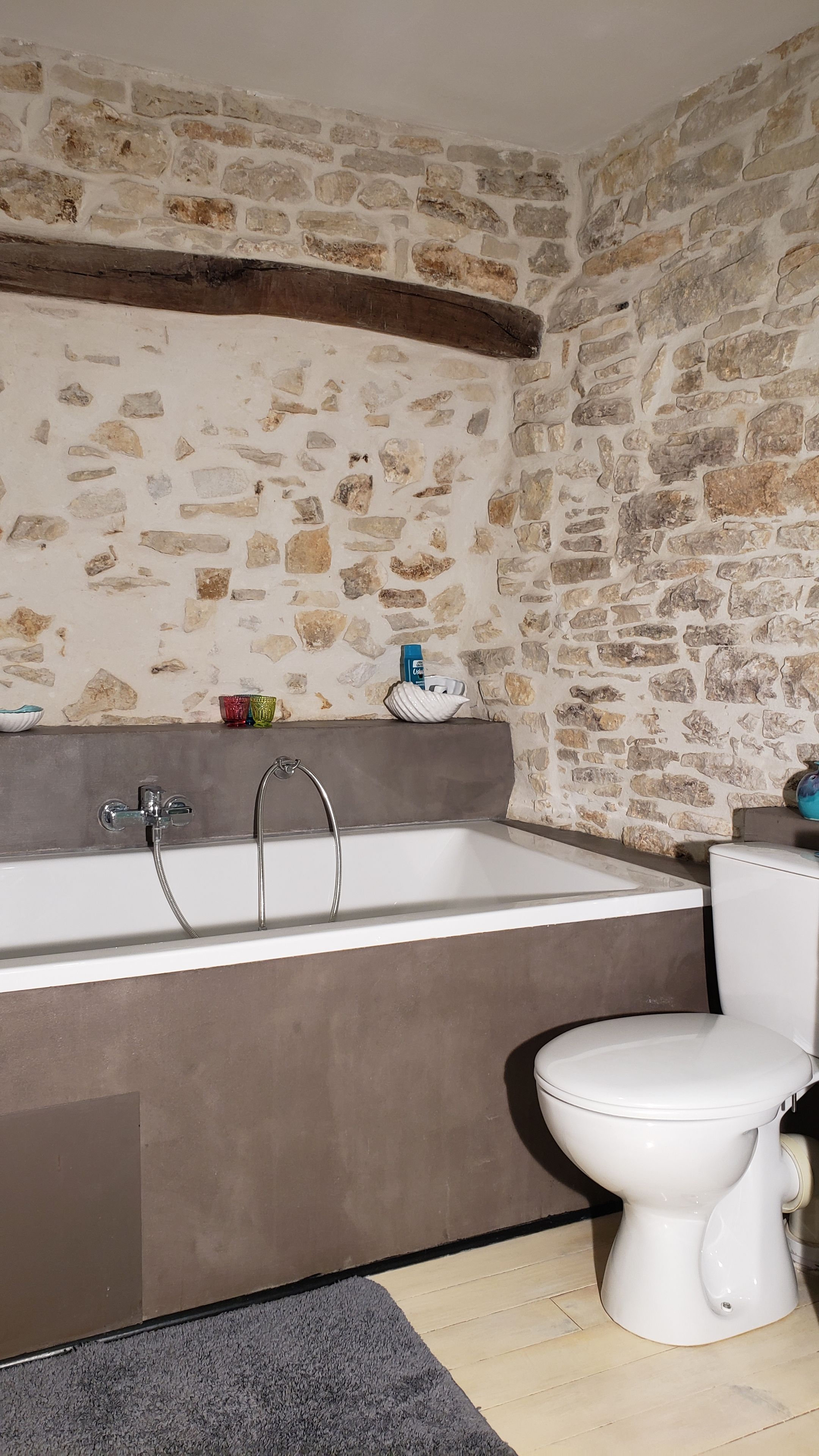 Un bagno con parete in pietra, una vasca, un water e un piccolo ripiano con oggetti decorativi.