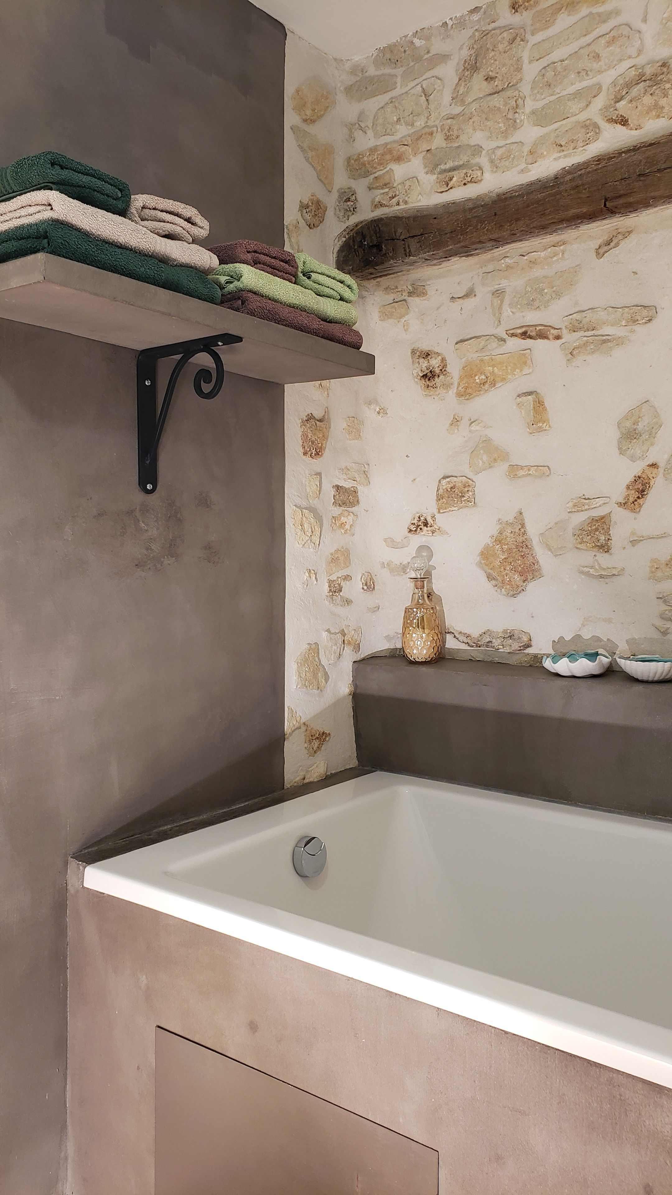 A bathroom with a bathtub, a towel rack with folded towels, a stone wall, and a decorative bottle.