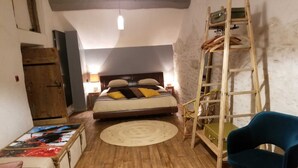 Una camera da letto con pavimento in legno, un letto con cuscini, una sedia blu, una scala e un armadio in legno.