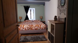 A bedroom with a bed, a nightstand, a dresser, a window with curtains, and a wall-mounted mirror. - L'autre Bout de Toit (Meursault)