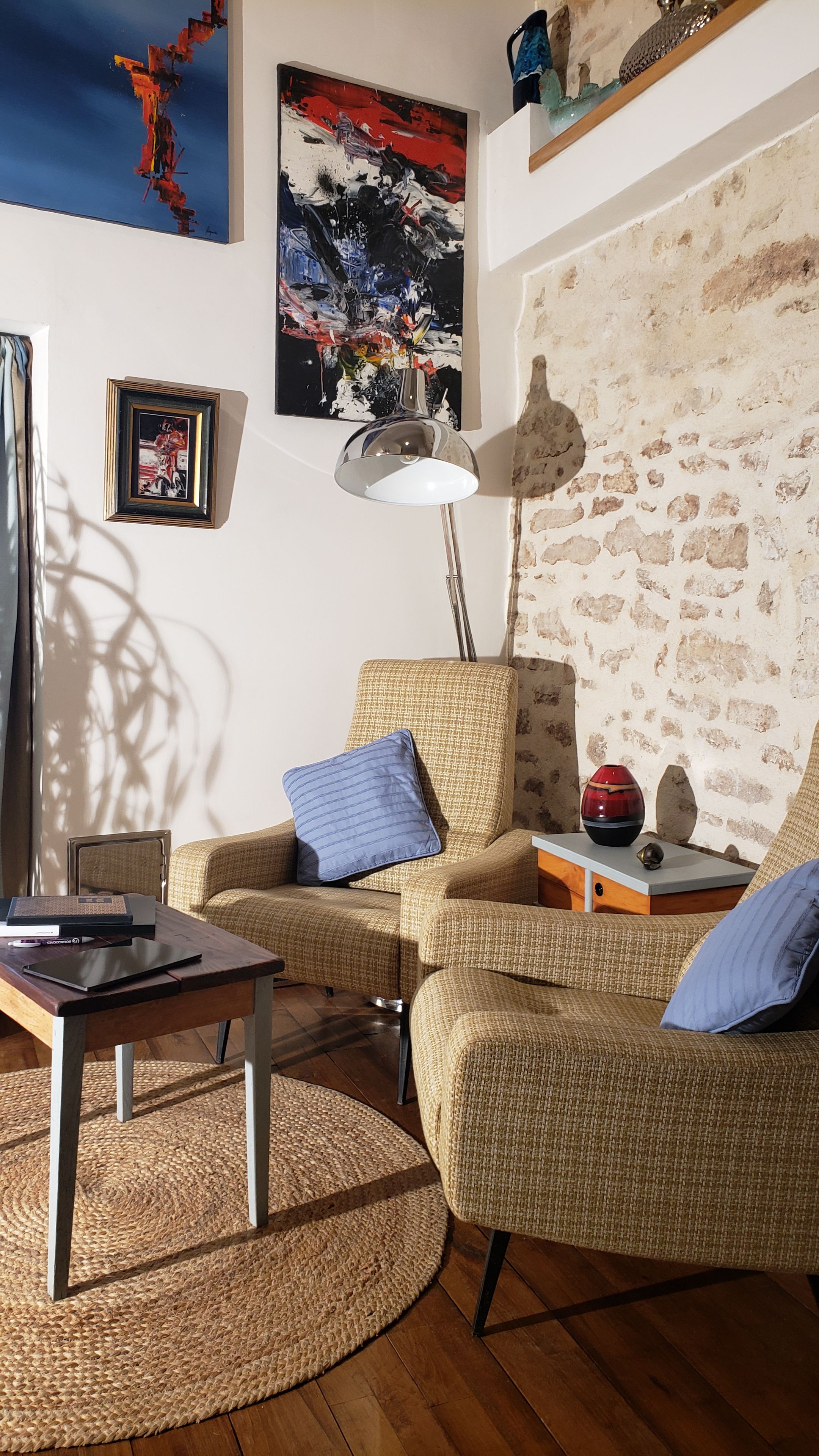 A cozy living room with a round woven rug, a sofa with blue cushions, a small table with a laptop, and a floor lamp.
