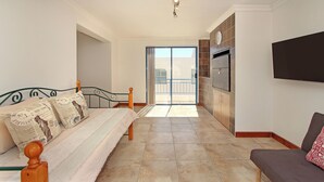 Een slaapkamer met een bed, een bank, een televisie en een schuifdeur naar een balkon.