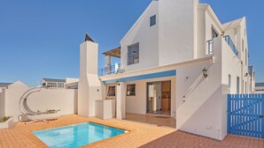 Een modern huis met twee verdiepingen, een zwembad, een overdekt terras en een blauw hek.