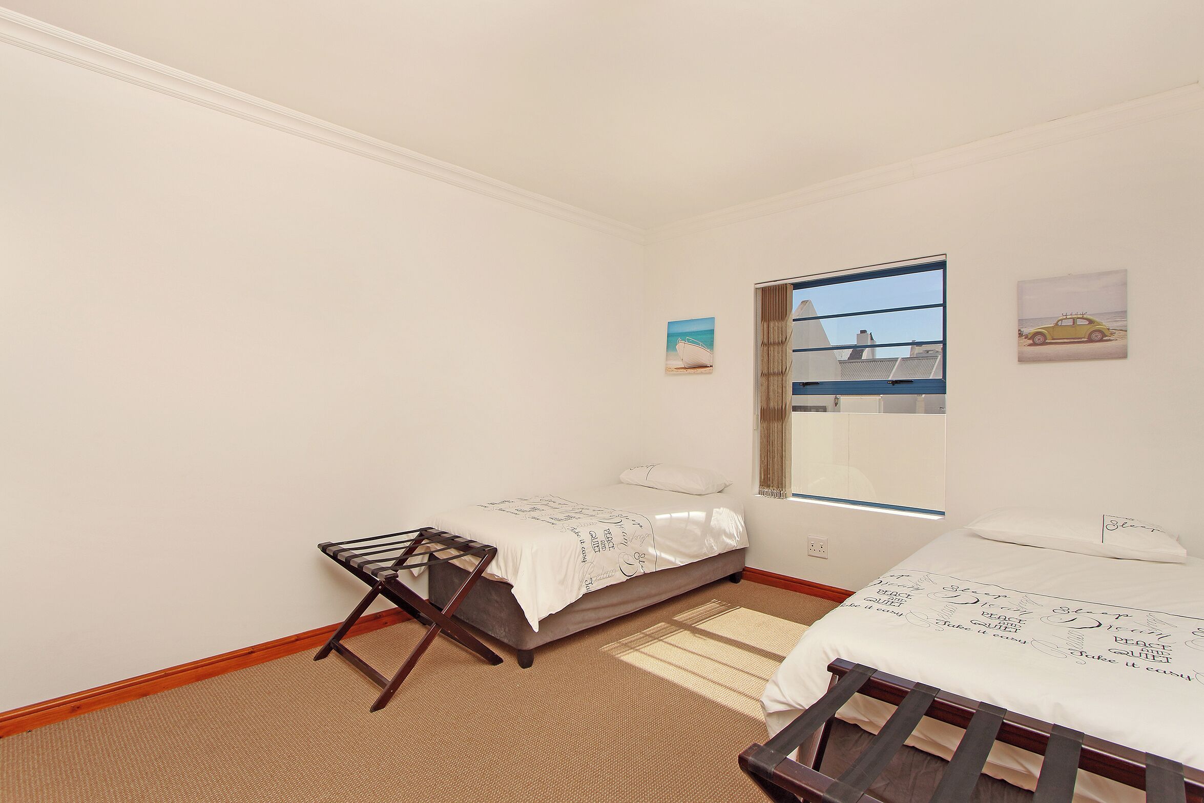 A bedroom with two beds, a window with a view, and a small painting on the wall.
