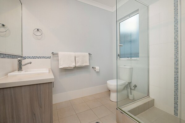 Une salle de bain moderne avec une douche à parois de verre, des toilettes blanches et un lavabo avec un miroir.