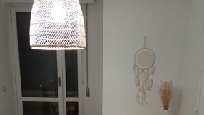 Een kamer met een grote geweven lamp, een dromenvanger en een rieten kast met een vaas droogbloemen.