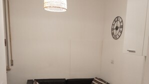 Een knus woongedeelte met een zwarte leren bank, een houten eettafel met een spoelbak en een hanglamp.