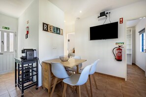 A dining area with a wooden table, light blue chairs, a black cart with shelves, a fire extinguisher, and a mounted TV.