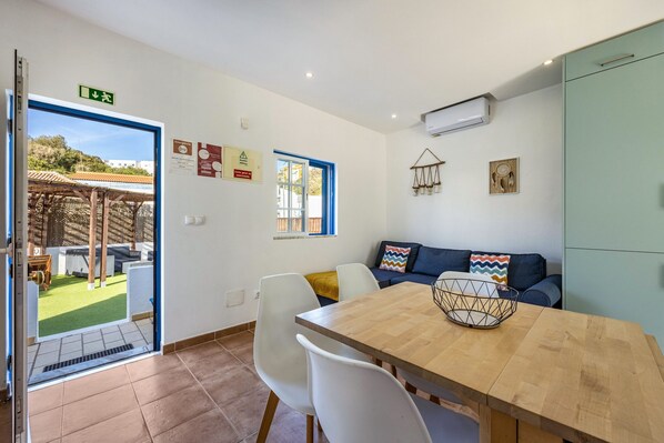 A modern kitchen with a wooden table, white chairs, a blue sofa, and a view of a garden.