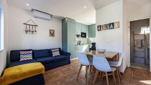 Ett kompakt bostadsutrymme med en soffa, ett matbord med stolar, en köksdel och en väggmonterad luftkonditioneringsanläggning.