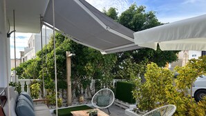 Une terrasse couverte, aménagée avec du mobilier d’extérieur, une table en bois et une chaise blanche.