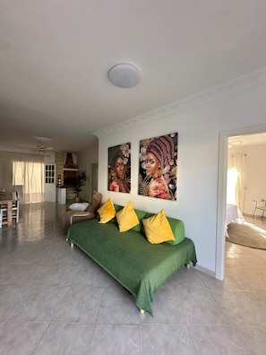 A spacious living area with a green sofa, yellow pillows, and two large floral paintings on the wall.