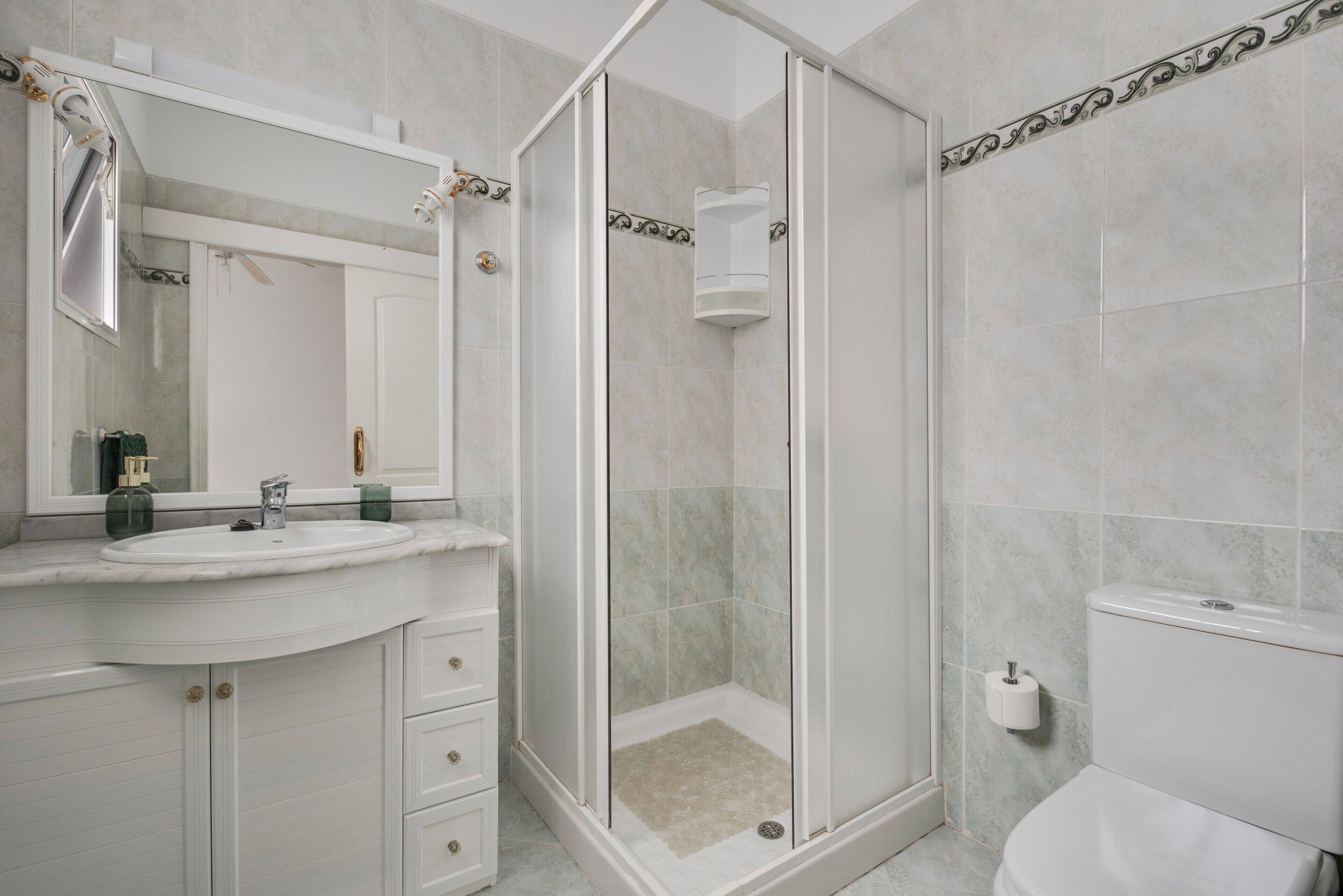 Un baño con cabina de ducha de vidrio, un lavabo con espejo y un inodoro.