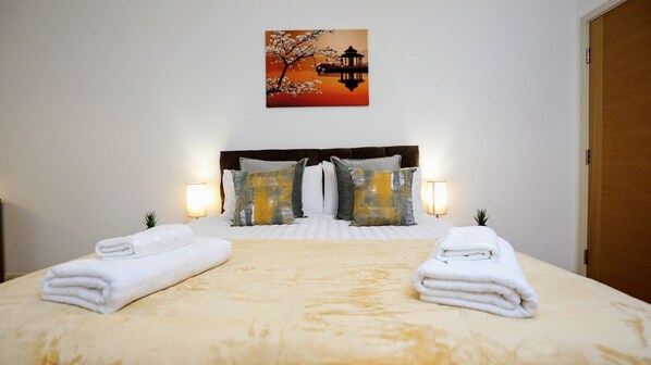 A neatly made bed with white linens and towels, a wooden headboard, and two bedside lamps.