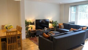 Ein modernes Wohnzimmer mit Sofa, Fernseher, Esstisch und Lampen.