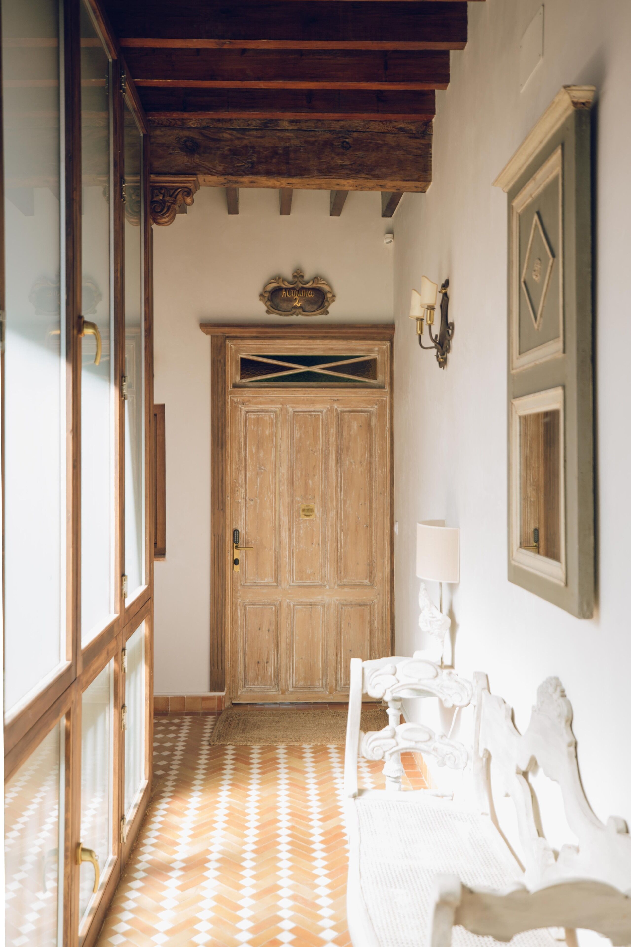 A hallway with a wooden door, a bench, and a wall-mounted lamp.