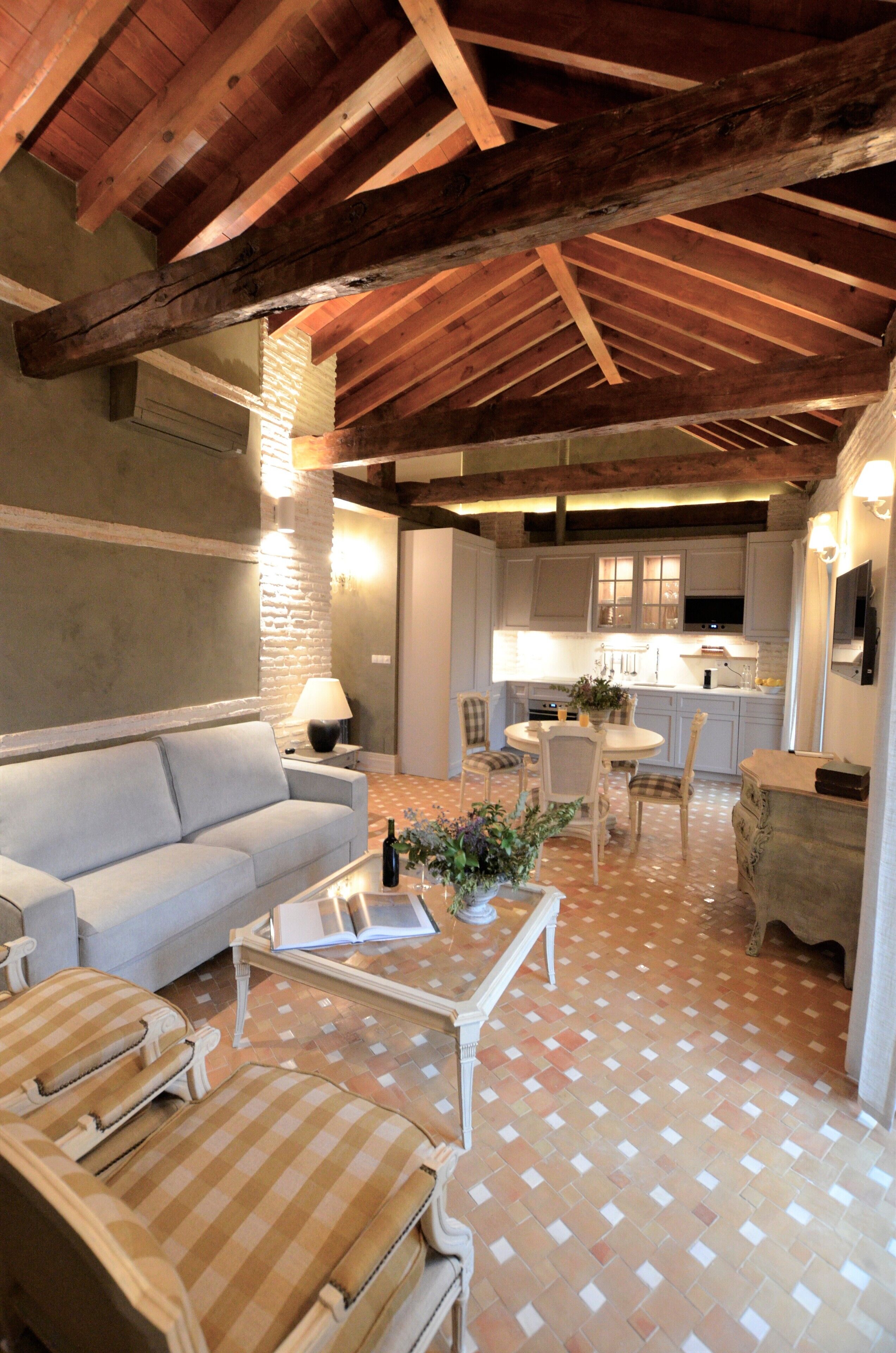 Una sala acogedora con un sofá, sillones, una mesa de centro y una mesa de comedor. Se ve una cocina al fondo, con armarios y un televisor.