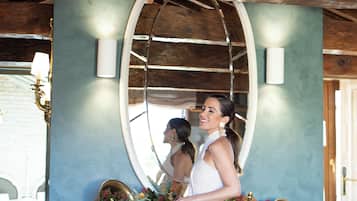 Una mujer con vestido blanco de pie frente a un espejo con una consola decorativa.