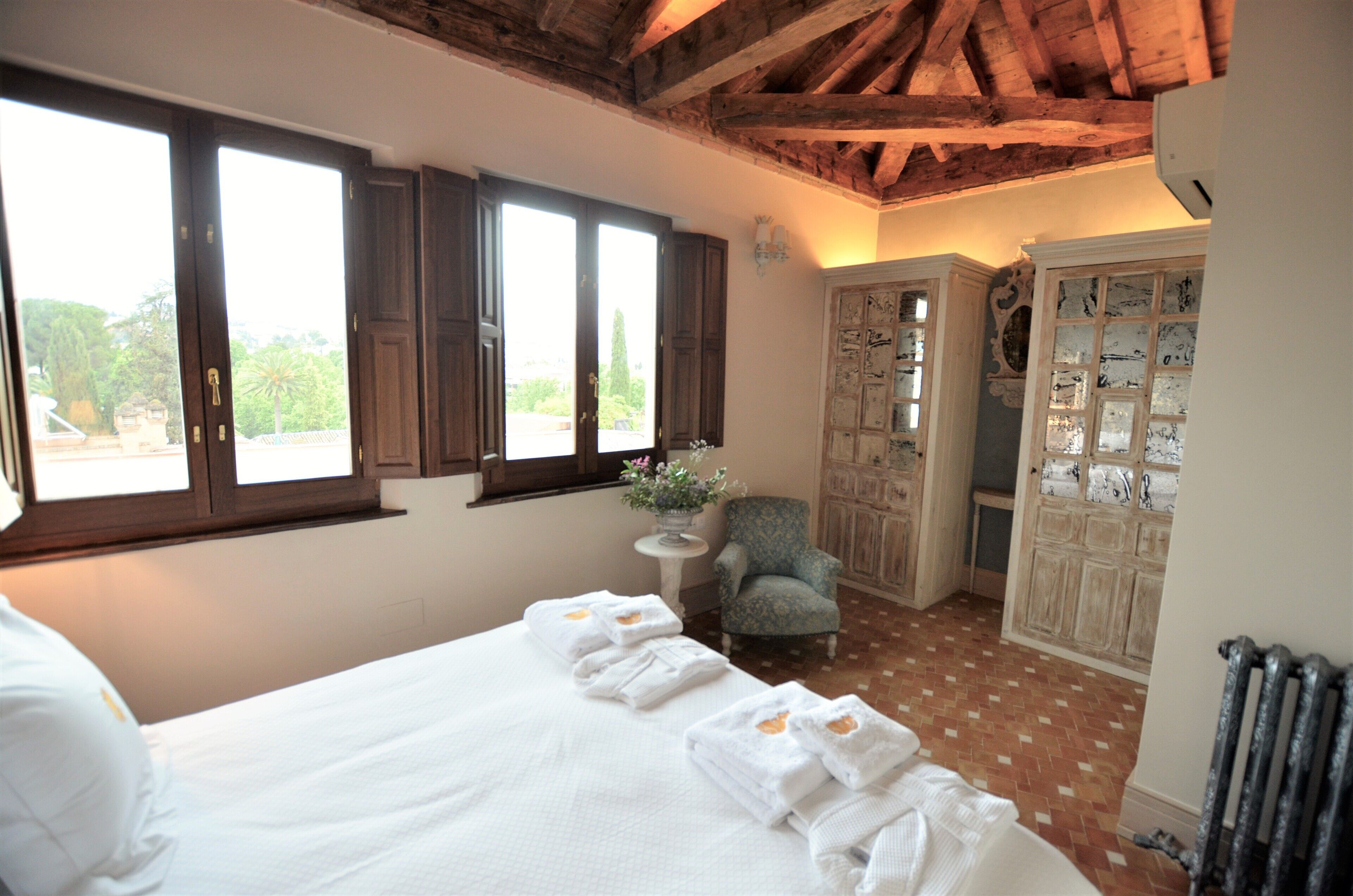 Een slaapkamer met een groot bed, een stoel, een klein tafeltje met een vaas en een kledingkast met decoratieve panelen.