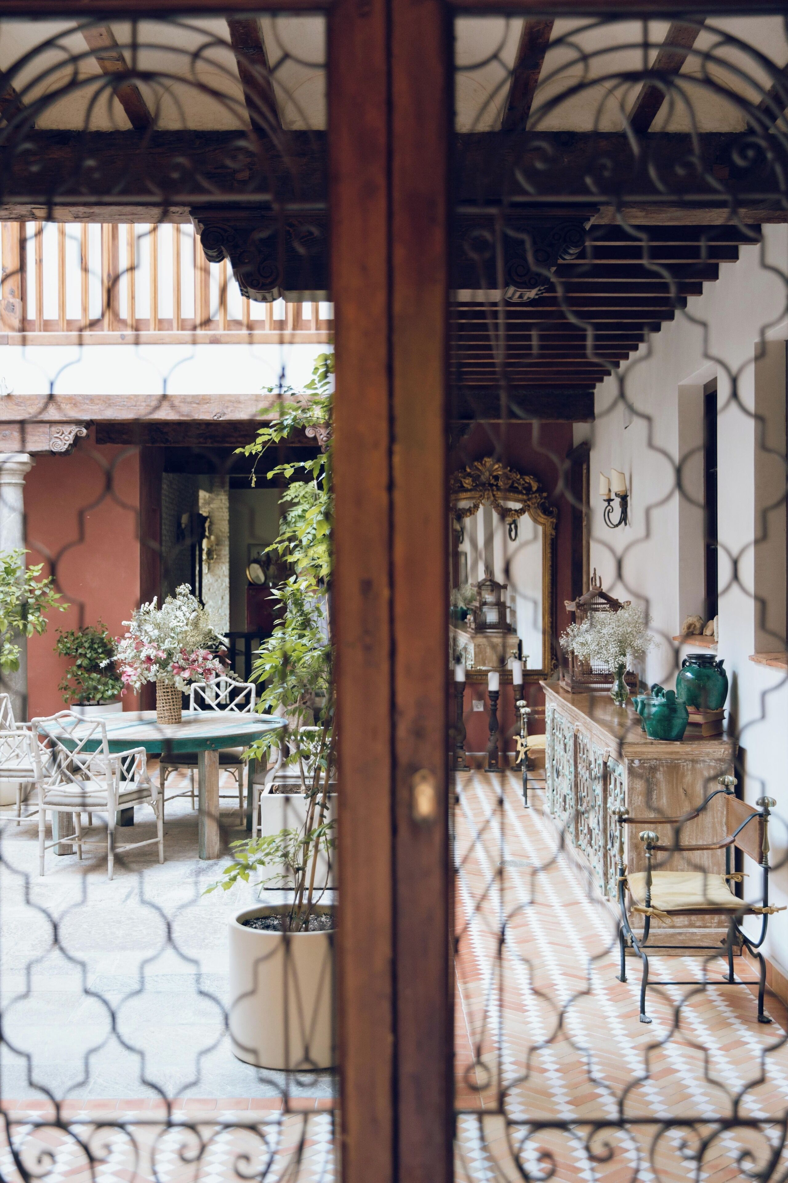 A courtyard with a wooden pergola, a dining table with chairs, potted plants, and a decorative mirror.