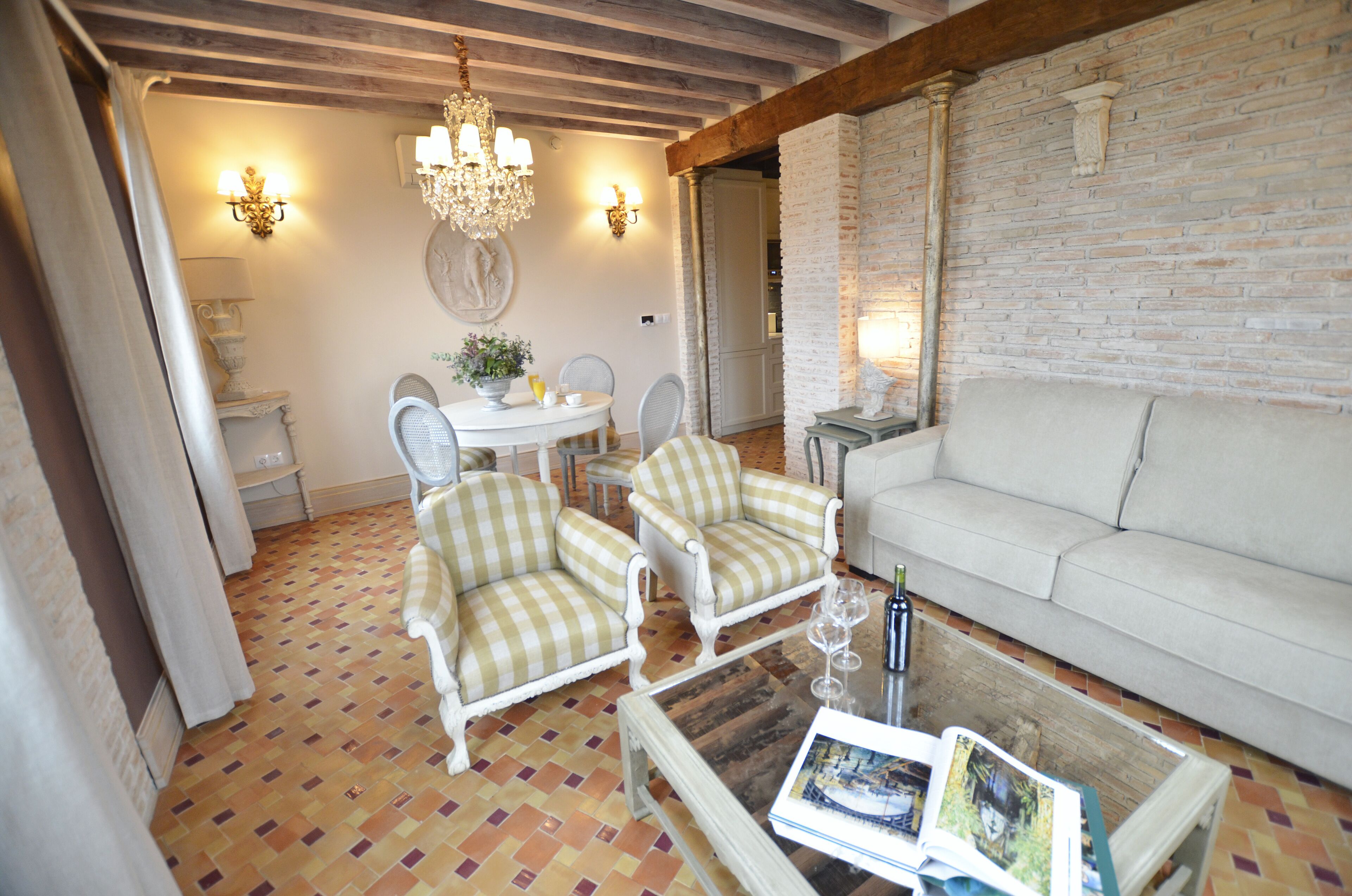 Un salon chaleureux avec un canapé blanc, deux fauteuils à rayures, une table basse ronde et un lustre.