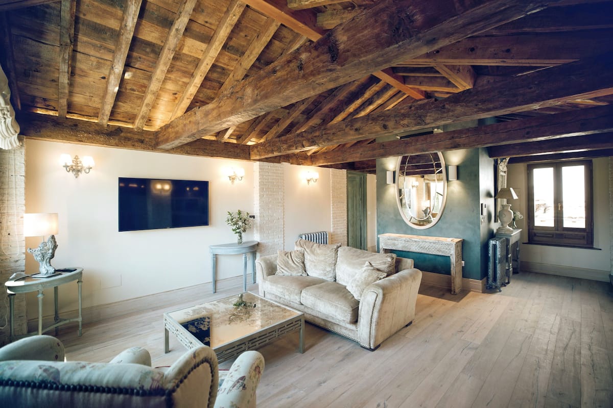 Ein gemütliches Wohnzimmer mit Holzbalkendecke, einem beigefarbenen Sofa, einem Couchtisch und einem Kamin.