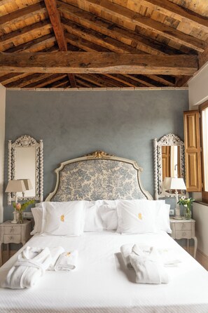 A neatly made bed with white linens and towels, a classic headboard, and wooden beams on the ceiling. - La Corrala del Realejo (Granada)