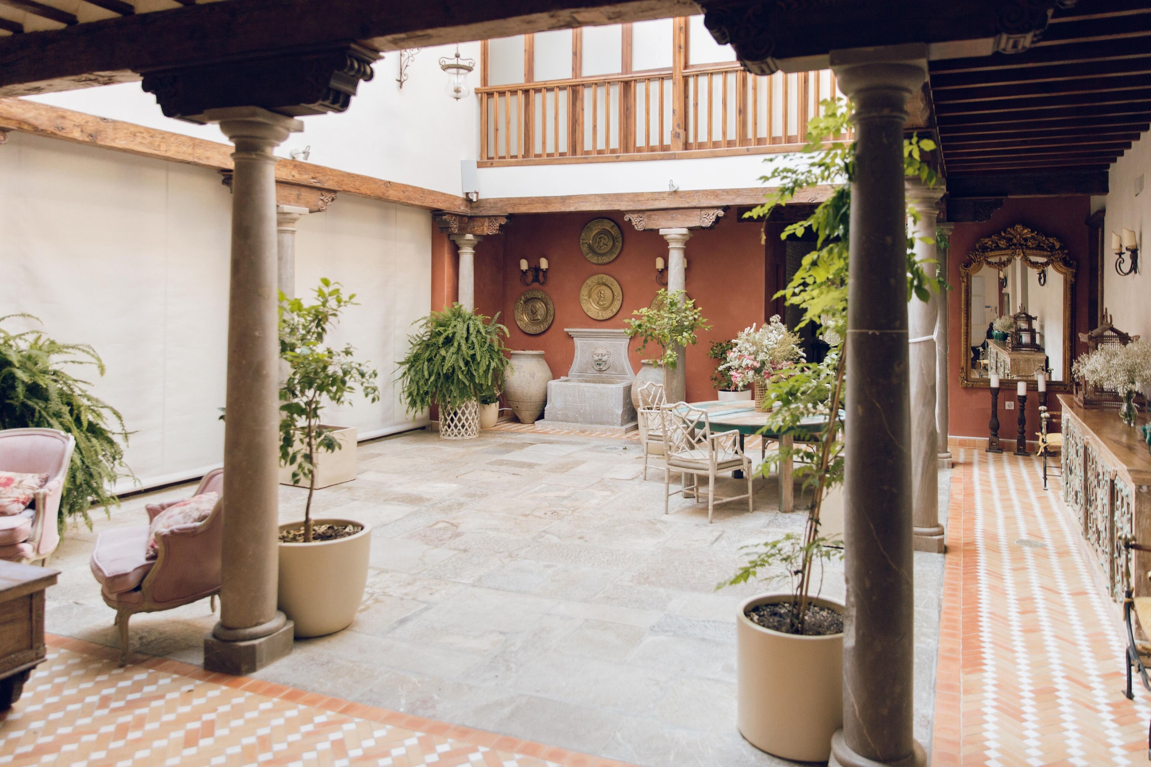 A courtyard with a wooden balcony, potted plants, and a tiled floor.