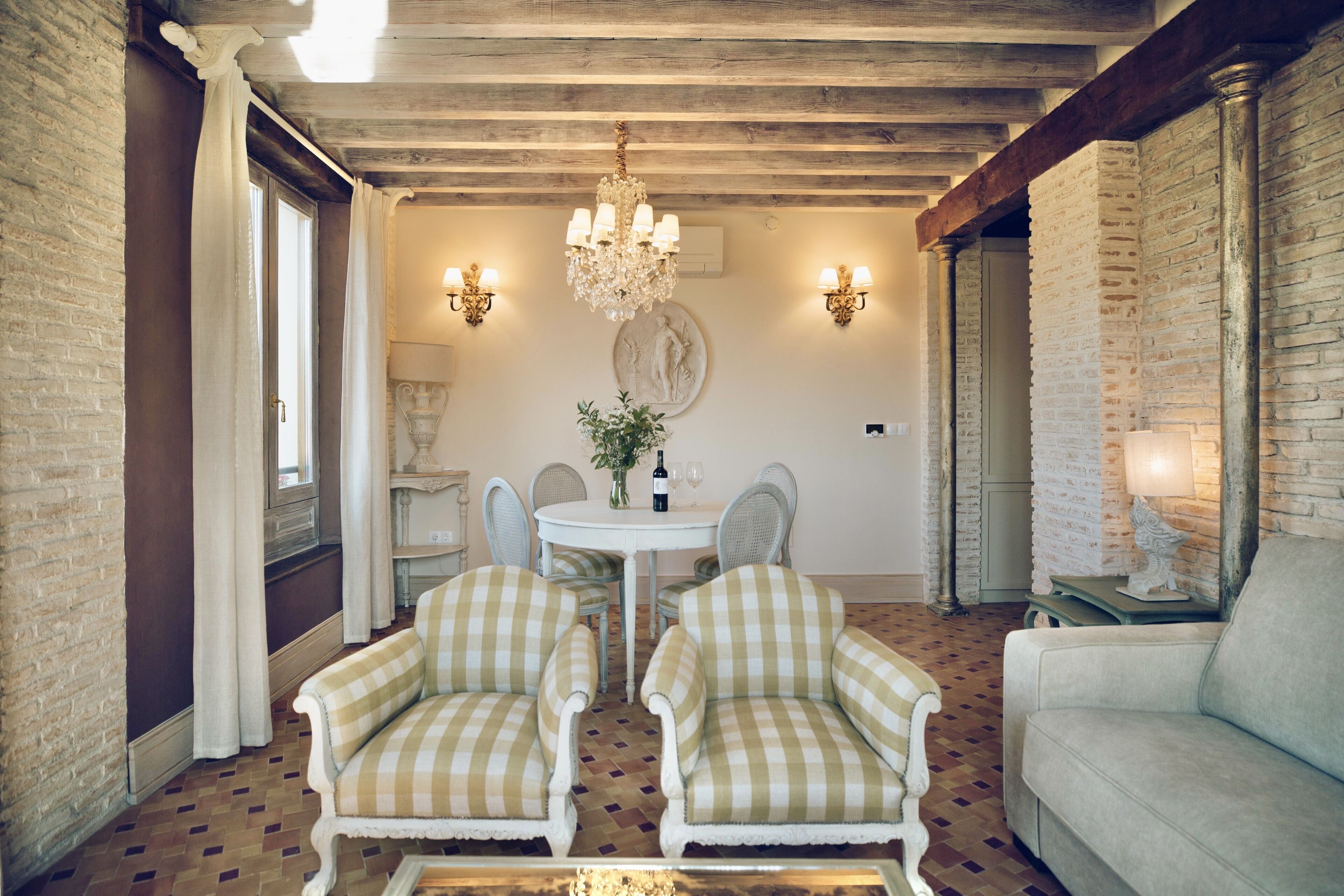 Une pièce avec un canapé à motifs à carreaux, une table ronde entourée de chaises, un lustre et des appliques murales.