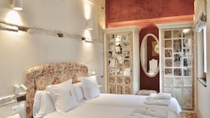 Una habitación de hotel con una cama grande, un cabecero floral, un aparador de madera con puertas de cristal y una pared de acento roja.