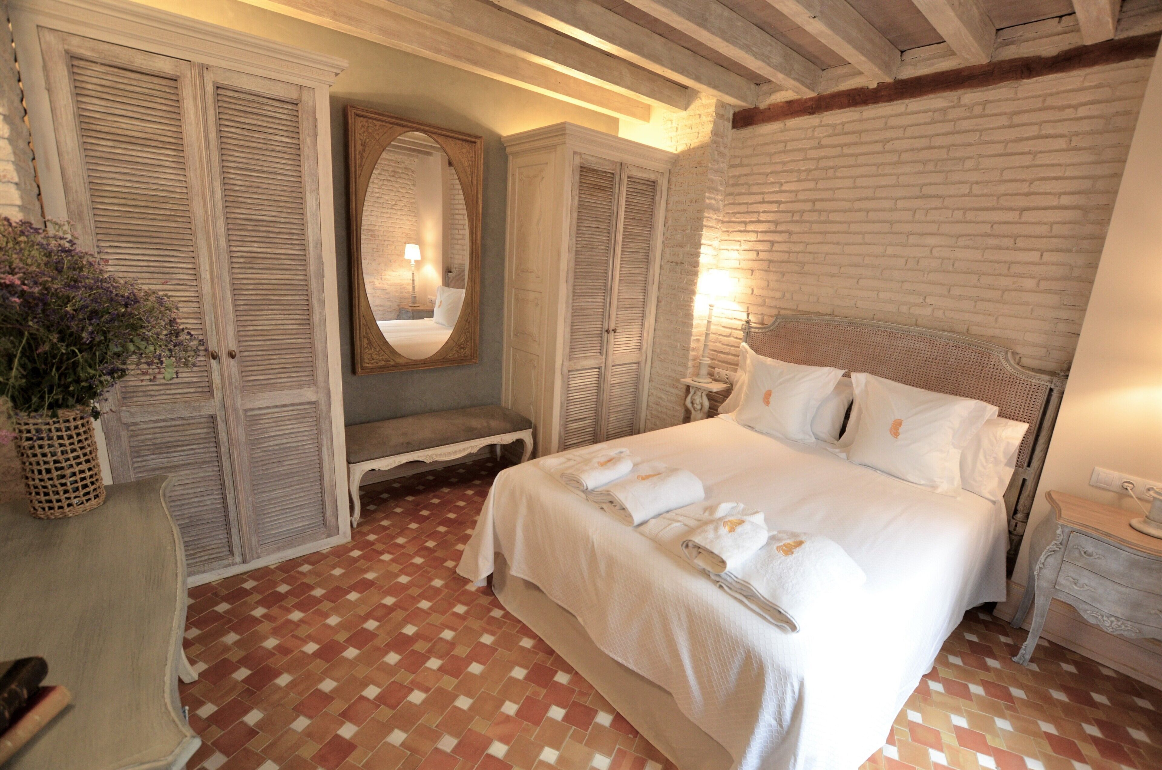 Un dormitorio con una cama grande, un banco, un espejo y una pared de ladrillo.