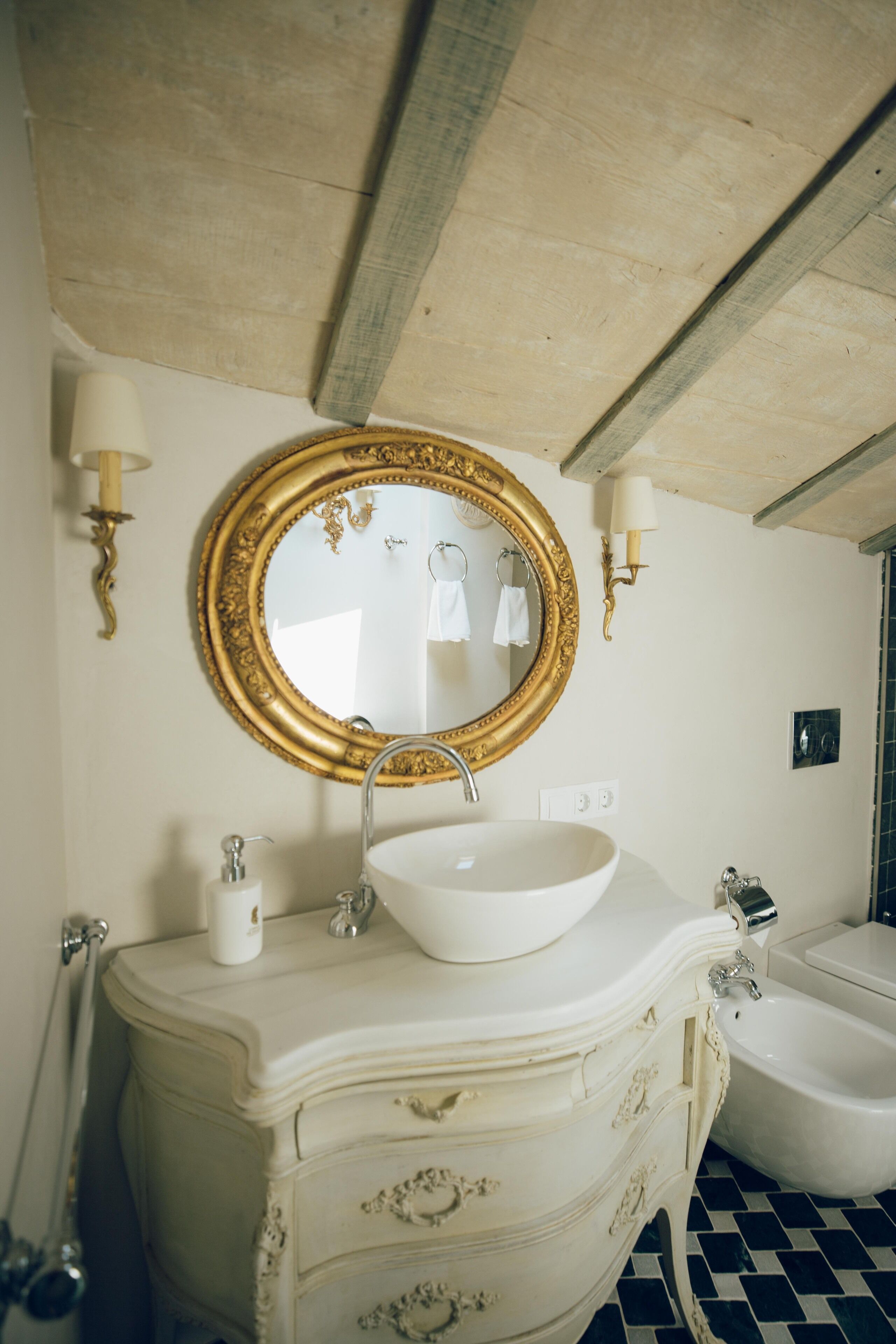 A bathroom with a white sink, gold-framed mirror, and a bathtub.