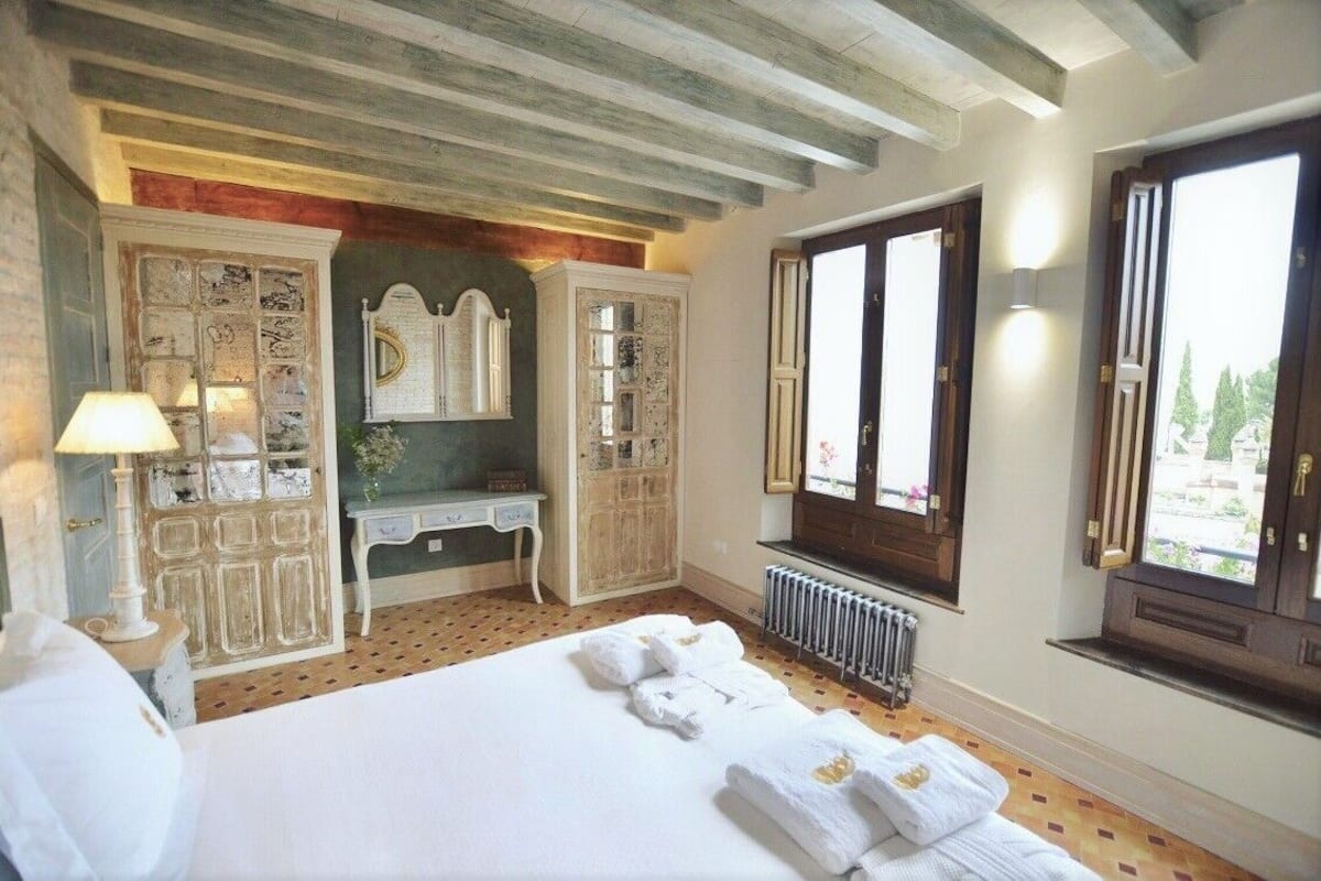 Ein Hotelzimmer mit einem großen Bett, einem Schminktisch mit Spiegel, einem Fenster mit Blick und einer Heizung.