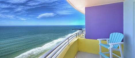 A balcony with a view of the ocean, a purple wall, and a blue chair.