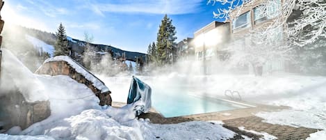 Zona exterior cubierta de nieve con piscina, muros de piedra y cielo despejado.