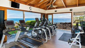 Ein Fitnessraum mit Laufbändern, Ergometer und Rudergerät mit Blick auf eine malerische Meereslandschaft.