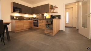 A modern kitchen with wooden cabinets, a built-in oven, and a dining area with a table and chairs. - Ferienhaus am Angerplatz (Cuxhaven)