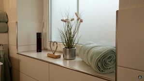 A bathroom with a window, a towel, a plant, and a heart-shaped decoration on the counter. - Ferienhaus am Angerplatz (Cuxhaven)