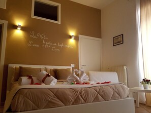 Une chambre d’hôtel avec un lit, des oreillers, une table de chevet ornée d’un vase de fleurs et un mur muni d’un luminaire et d’un tableau encadré.