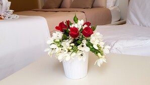 Habitación de hotel con una cama, una mesita de noche con un florero y una pared con un cartel.