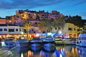 Un port de plaisance avec des bateaux amarrés, un bâtiment situé au bord de l’eau et des palmiers.