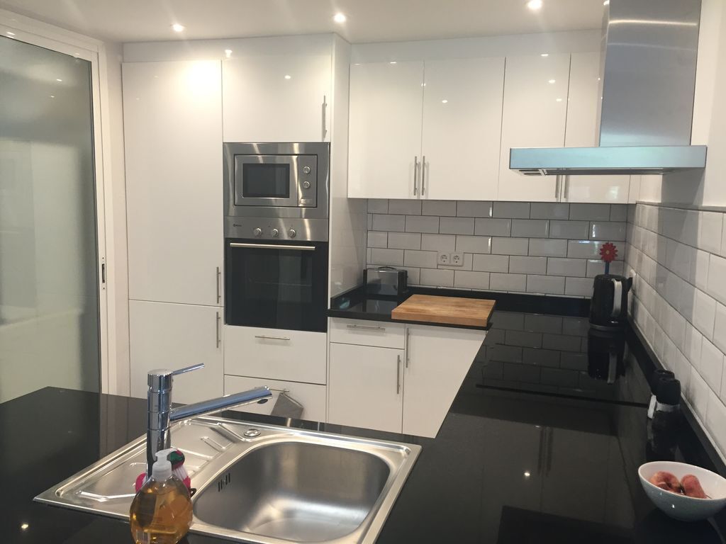 A modern kitchen with white cabinets, a stainless steel sink, a microwave, and a stove.