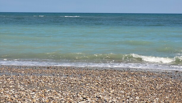 Una playa pedregosa con olas marinas tranquilas y cielos despejados.