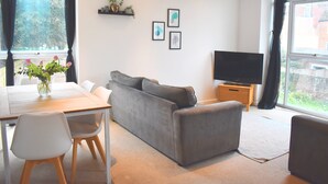 Una sala de estar moderna con un sofá, un televisor, una mesa de comedor con sillas y una ventana con cortinas.