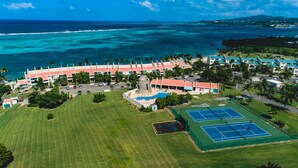 Vue aérienne d’un complexe hôtelier doté d’une grande piscine, de courts de tennis et offrant une vue sur l’océan.