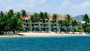 Un hôtel situé en bord de mer, avec plusieurs étages, des palmiers et une plage de sable.
