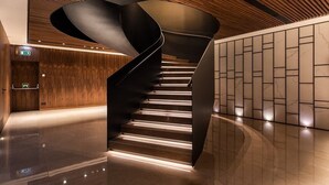 Una escalera en espiral moderna con escalones iluminados, paneles de madera en las paredes y suelo pulido.