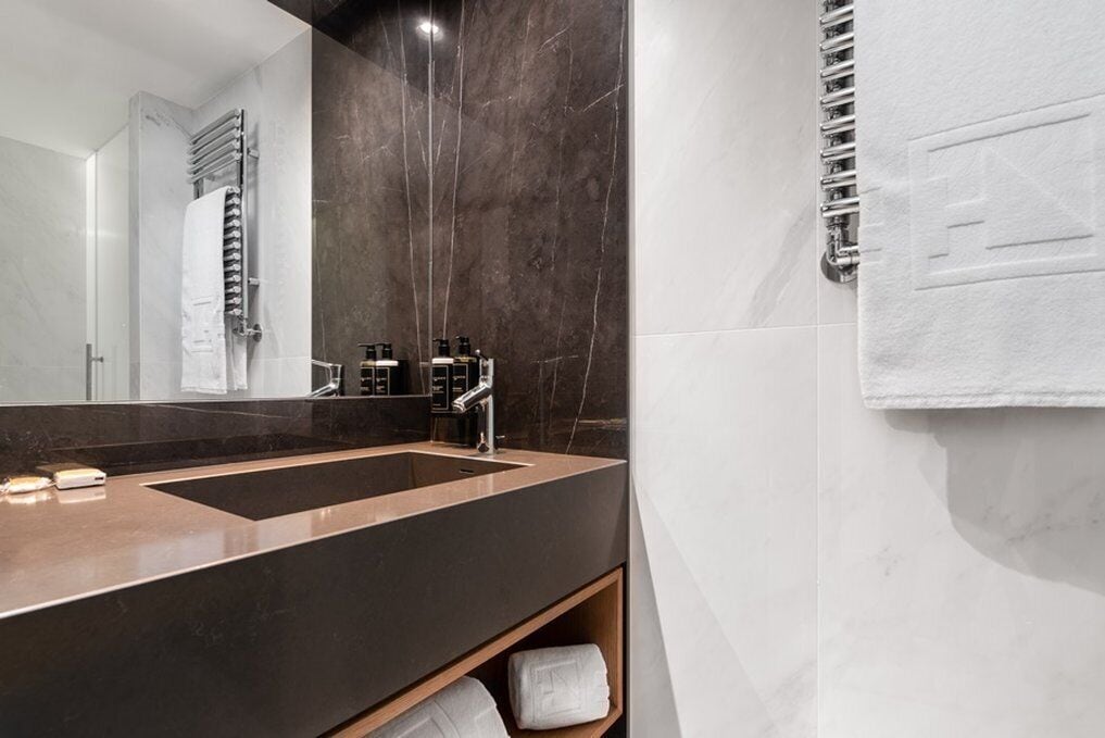 A modern bathroom with a large mirror, dark marble walls, a dual sink vanity, and a towel rack.